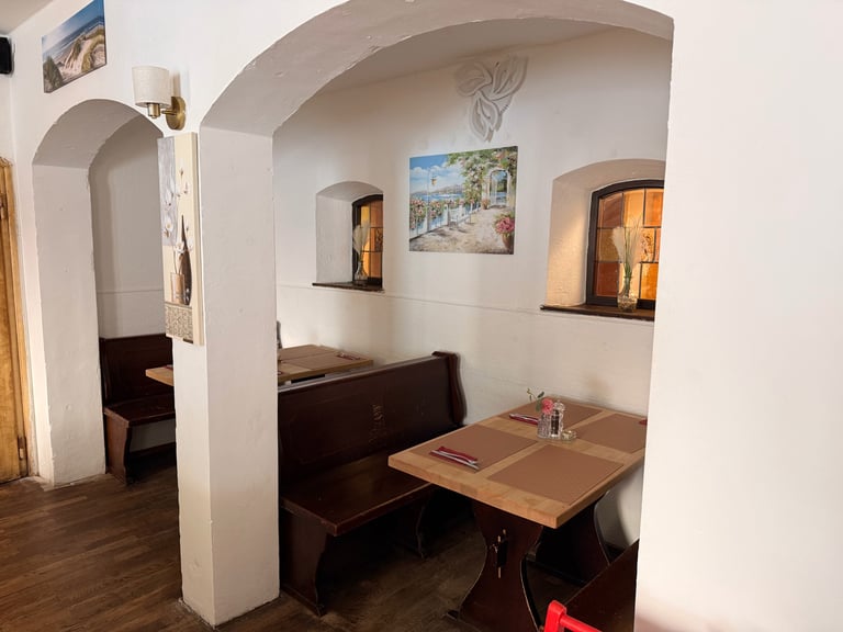 Cozy restaurant booth with dark wooden seating, small table, and arched white ceiling alcove with framed artwork on walls