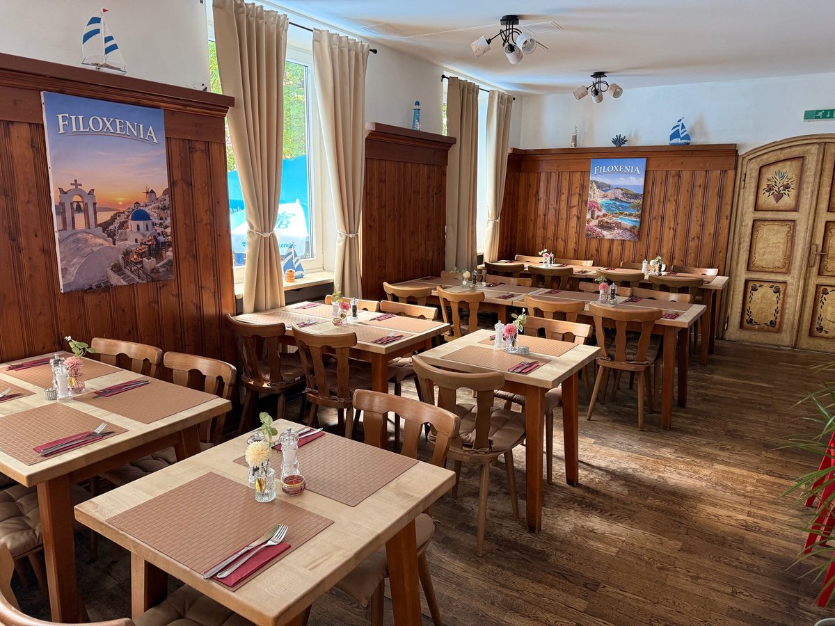 Upscale restaurant dining room with wooden tables, chairs, and decor featuring Mediterranean artwork and large windows
