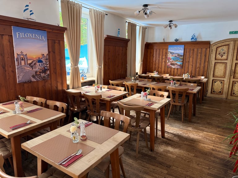 Upscale restaurant dining room with wooden tables, chairs, and decor featuring Mediterranean artwork and large windows