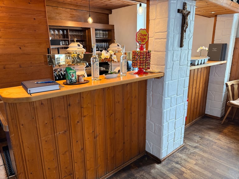 Wooden reception desk in a rustic room with shelves, decorative items, and a light blue door visible in the background