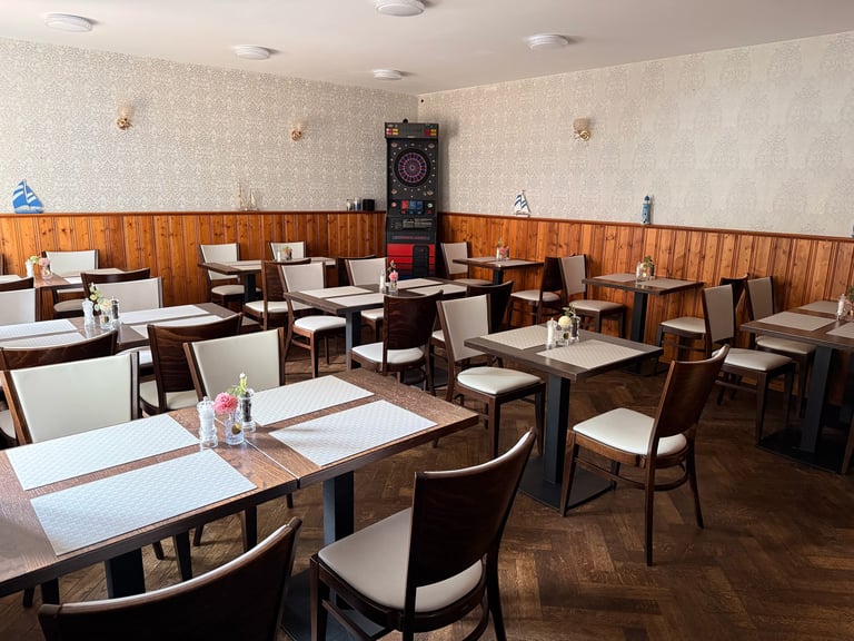 Empty dining room with wooden tables and chairs, beige wallpaper, wood paneling, and a dartboard on the back wall