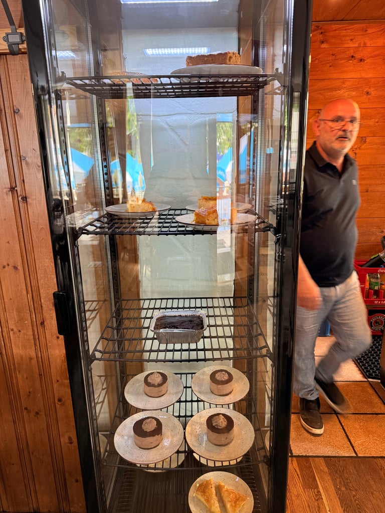 A glass display cabinet filled with freshly baked bread and pastries on shelves, with a man in black shirt standing beside it